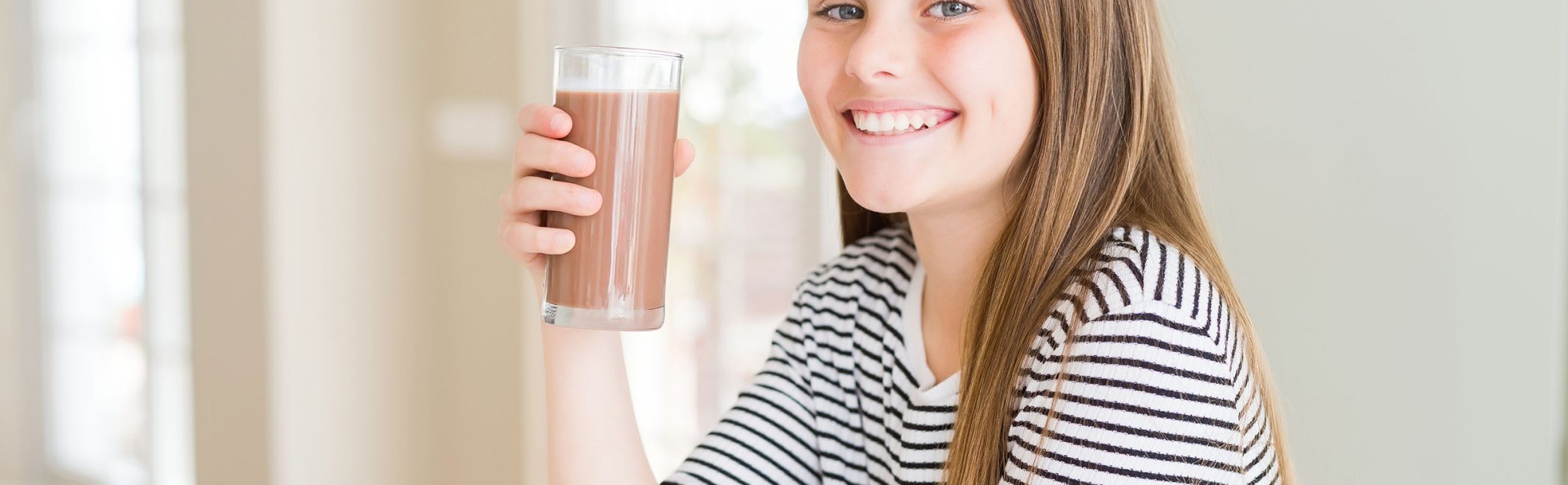 Beautiful young girl kid drinking fresh tasty chocolate milkshake as snack with a happy face standing and smiling with a confident smile showing teeth